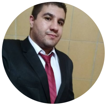 Foto do Eduardo de terno preto e gravata vermelha com fundo de azulejos amarelo